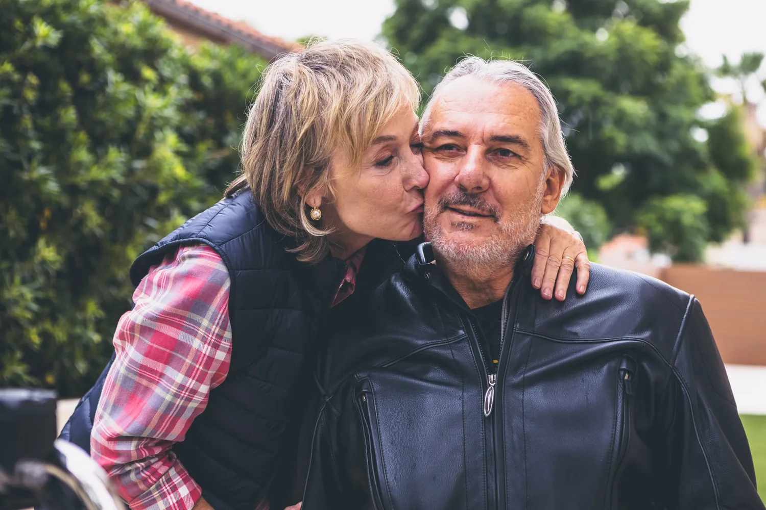 A mature woman kisses a man's cheek outdoors, suggesting affection after heartbreak without a fixed timetable